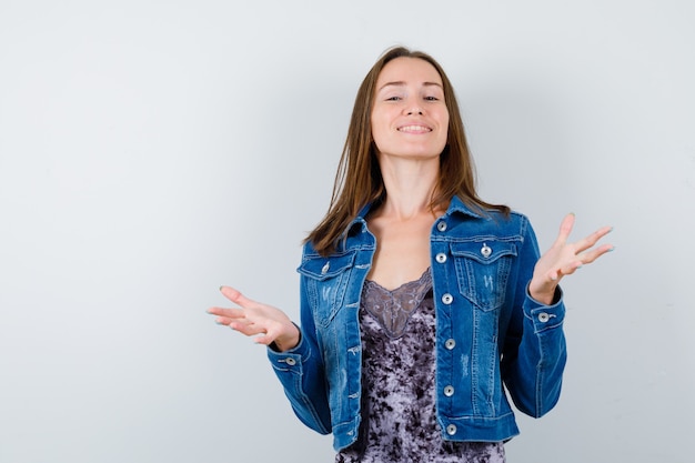 Young lady in blouse, denim jacket pretending to hold something and looking happy , front view.