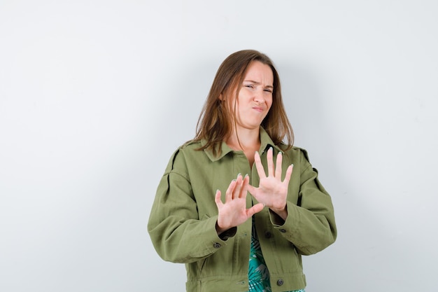 Young lady in blouse, jacket showing stop gesture and looking displeased , front view.