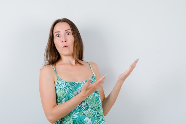 Young lady in blouse welcoming something and looking puzzled , front view.