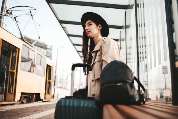 Young lady in coat and hat sits at a bus city stop