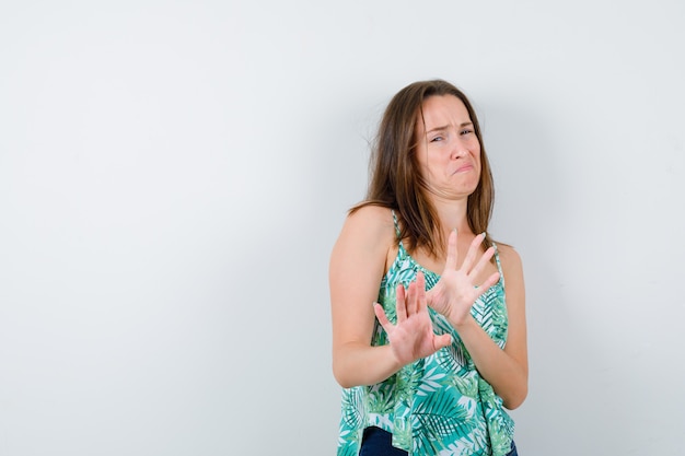 Young lady keeping hands to defend herself in blouse and looking scared. front view.