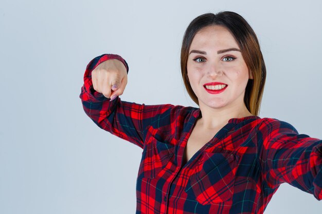 Young lady pointing forward in checked shirt and looking merry. front view.