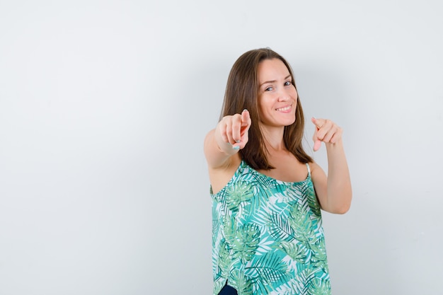 Young lady pointing forward and looking merry , front view.