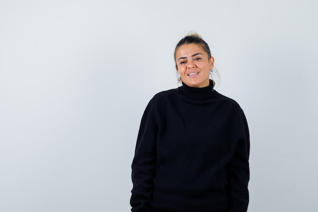 Young lady posing while looking at camera in black sweater and looking cheery. front view.