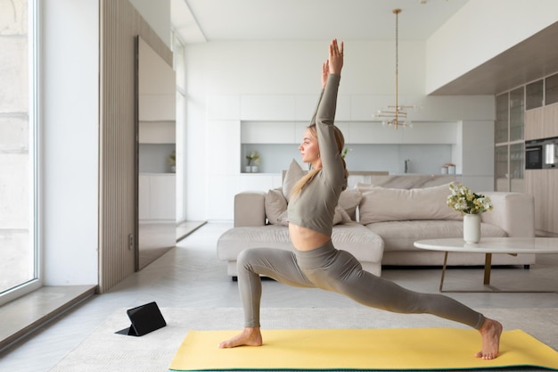 Young lady practices yoga at home with tablet pc