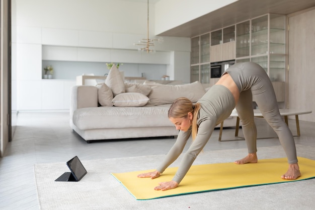 Young lady practices yoga at home with tablet pc