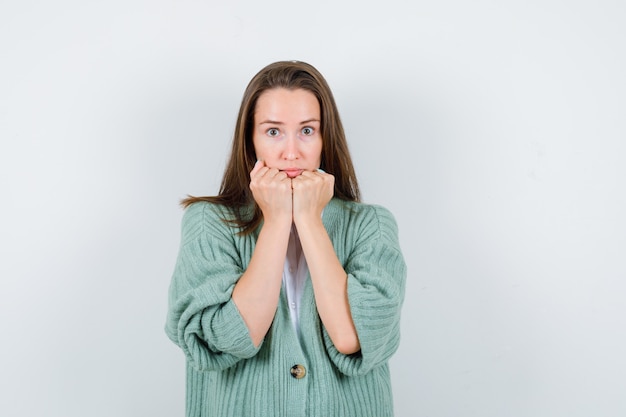 Young lady propping chin on fists in shirt, cardigan and looking careful , front view.