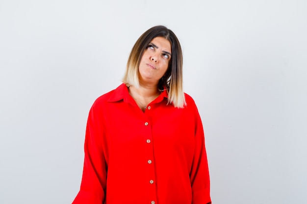 Young lady in red oversize shirt looking aside and looking thoughtful , front view.