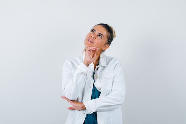 Young lady in shirt, white jacket with hand under chin and looking thoughtful , front view.