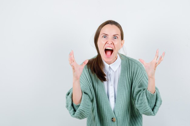 Young lady showing claws imitating a cat while screaming in blouse, cardigan and looking aggressive. front view.