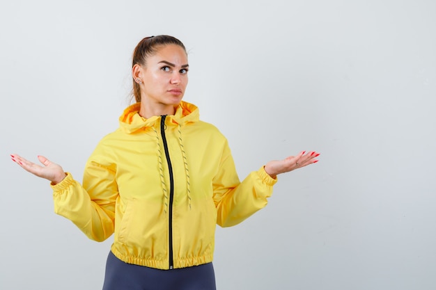 Young lady showing helpless gesture in yellow jacket and looking indecisive . front view.