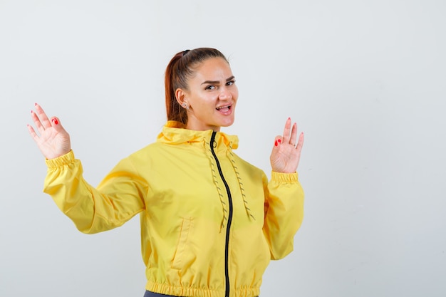 Young lady showing ok gesture in yellow jacket and looking joyful. front view.