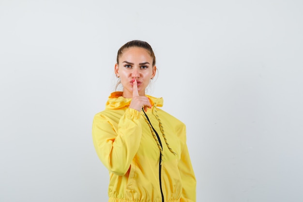 Young lady showing silence gesture in yellow jacket and looking confident , front view.