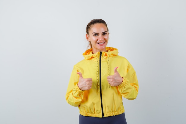 Young lady showing thumbs up in yellow jacket and looking optimistic. front view.