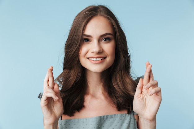 Young lady standing isolated over blue making hopeful gesture.