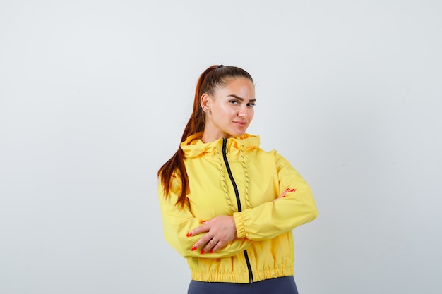 Young lady standing with crossed arms in yellow jacket and looking self-confident , front view.