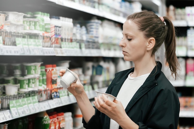 A young lady in the store chooses yogurt products reads and compares the composition on the labels The concept of healthy eating lowfat foods