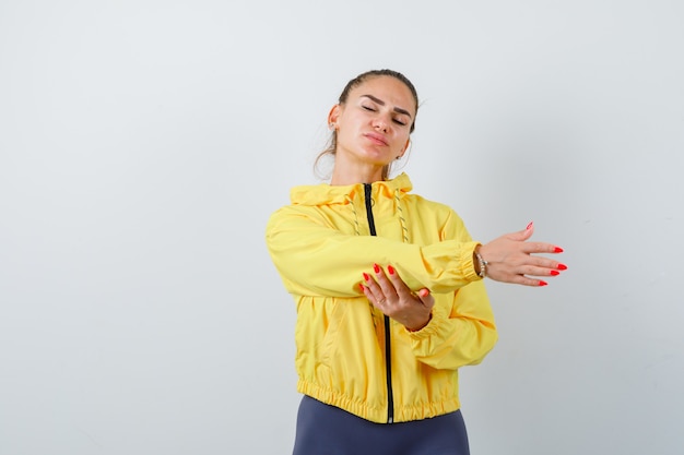 Young lady stretching hand aside in yellow jacket and looking relaxed , front view.