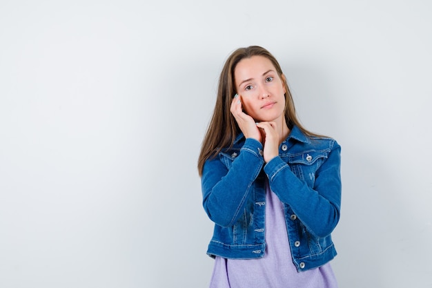 Young lady in t-shirt, jacket examining face skin on cheek and looking delicate , front view.