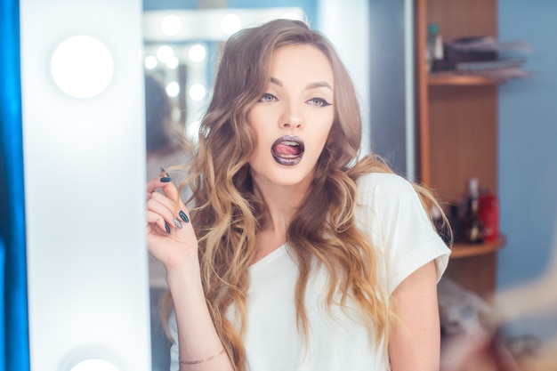 young lady with beautiful make up and curly hairstyle licks lips across the mirror