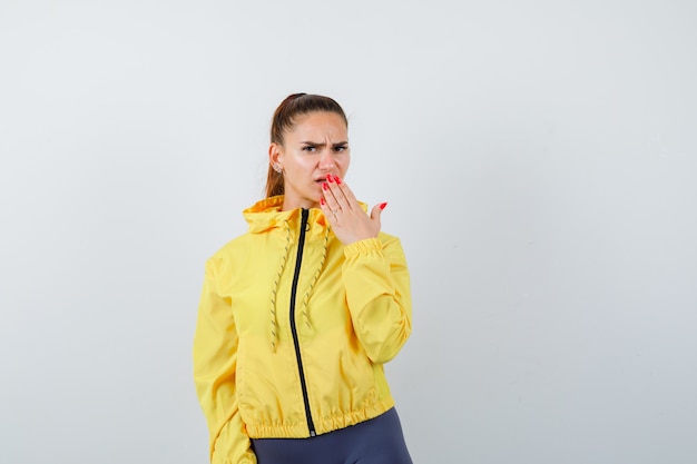 Young lady with hand on mouth in yellow jacket and looking anxious. front view.