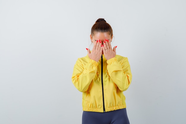 Young lady in yellow jacket covering face with hands and looking depressed , front view.