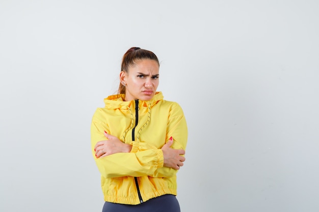 Young lady in yellow jacket hugging herself and looking dissatisfied , front view.