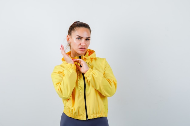 Young lady in yellow jacket scratching palm and looking dissatisfied , front view.