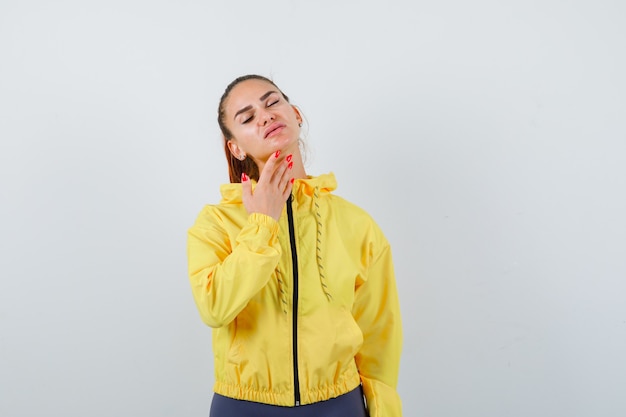 Young lady in yellow jacket with hand under chin and looking peaceful , front view.