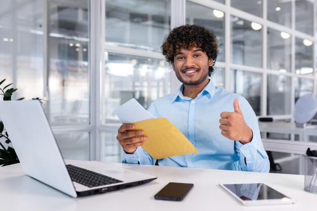 Photo a young latin american male student in sitting at a desk on campus holding an envelope with a letter