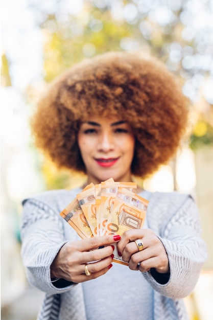 Young Latin American woman smiling happy holding money European euros in the city