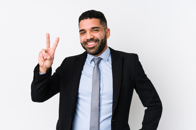 Young latin business woman against a white wall isolated showing victory sign and smiling broadly.