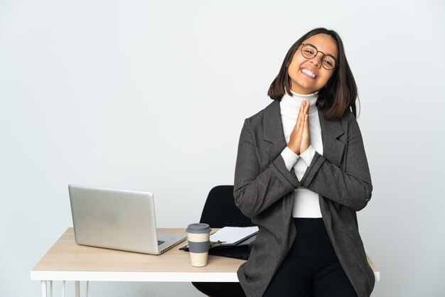 Young latin business woman working in a office isolated on white background keeps palm together. Person asks for something