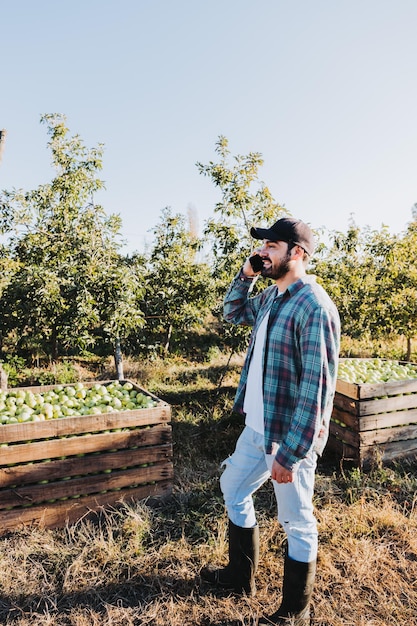 Young latin farmer man using his phone beside apple plantation Agricultural concept Digital nomad