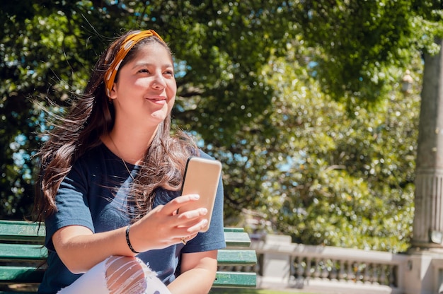 Young latin girl sitting in a park with mobile