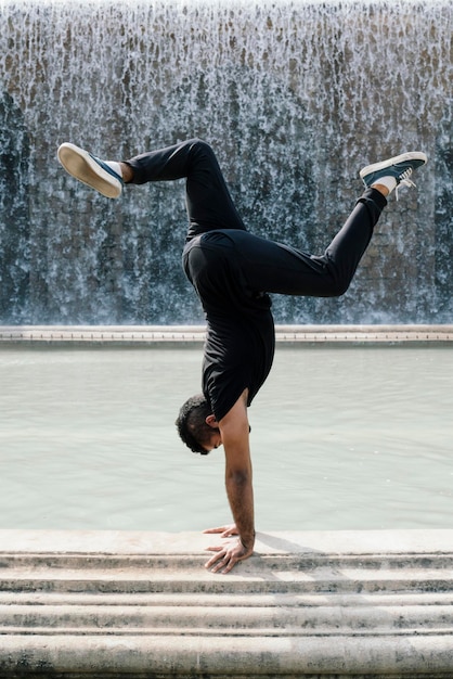 Photo young latin guy doing the vertical in front of a fountain in barcelona on a sunny day showing strength and determination