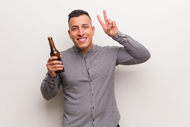 Young latin man holding a beer fun and happy doing a gesture of victory