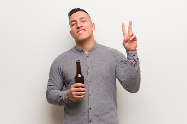 Young latin man holding a beer showing number two