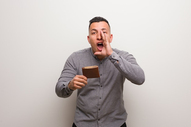 Young latin man holding a wallet shouting something happy to the front