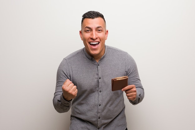 Young latin man holding a wallet surprised and shocked