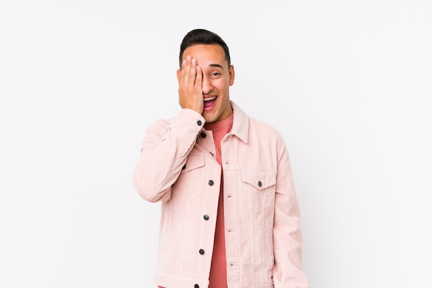 Young latin man posing isolated having fun covering half of face with palm.