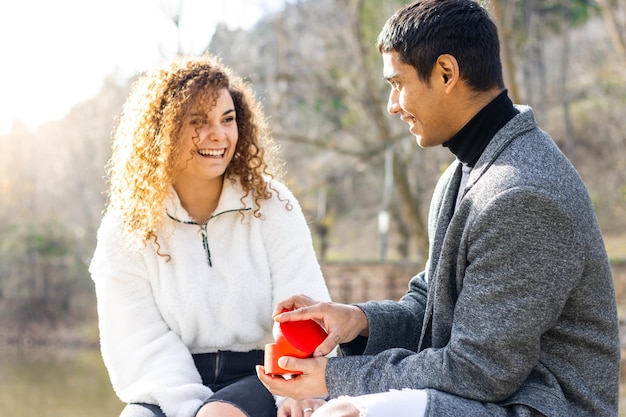 Young latin man proposing to his girlfriend outdoors Sitting guy making marriage proposal to smiling girlfriend