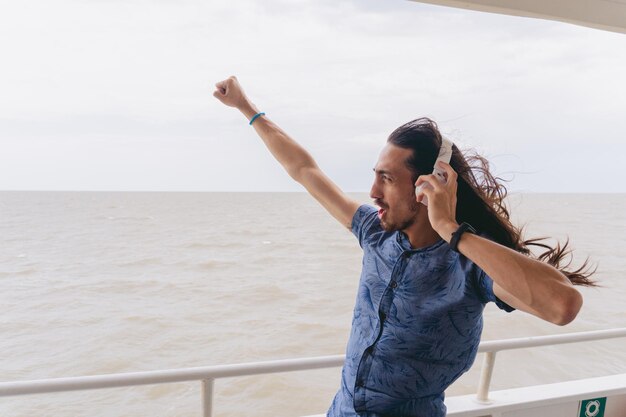 Young latin man with long hair wearing headphones while shouting with clenched fist towards the Rio de la Plata