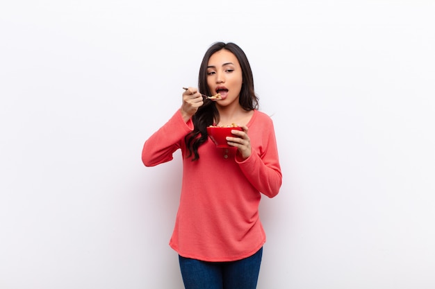 Young latin pretty woman against flat wall with a breakfast bowl