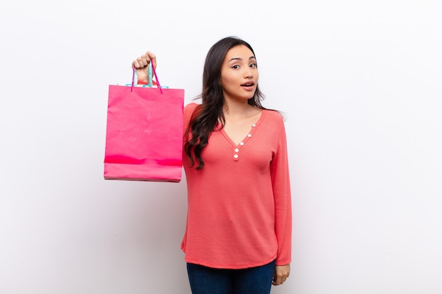 Young latin pretty woman  against flat wall with shopping bags