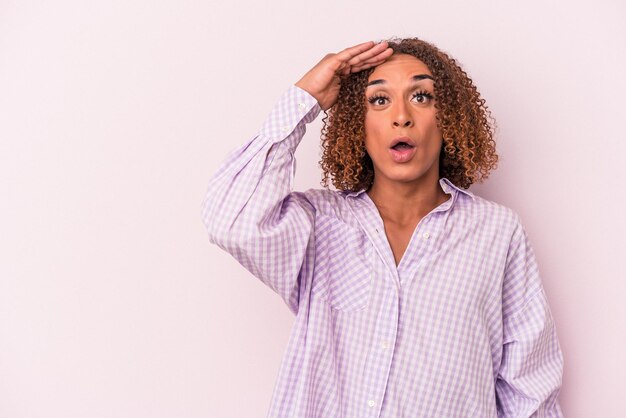 Young latin transsexual woman isolated on pink background looking far away keeping hand on forehead.