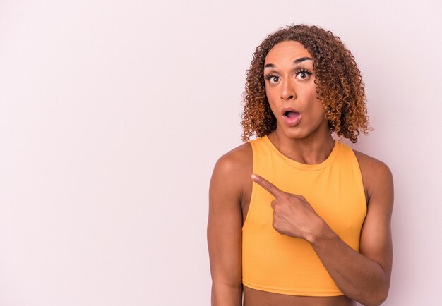 Young latin transsexual woman isolated on pink background pointing to the side