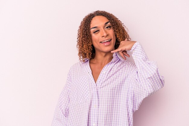 Young latin transsexual woman isolated on pink background showing a mobile phone call gesture with fingers.