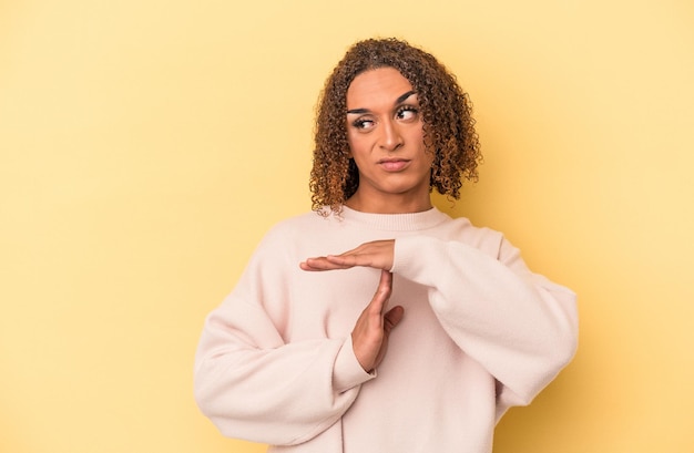 Young latin transsexual woman isolated on yellow background showing a timeout gesture.