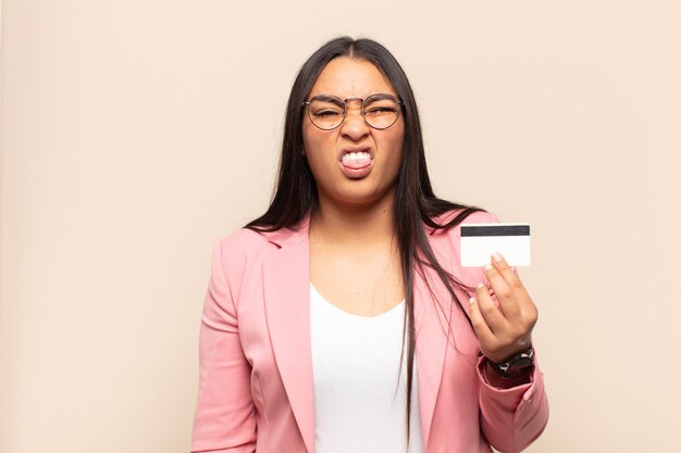 Young latin woman feeling disgusted and irritated, sticking tongue out, disliking something nasty and yucky